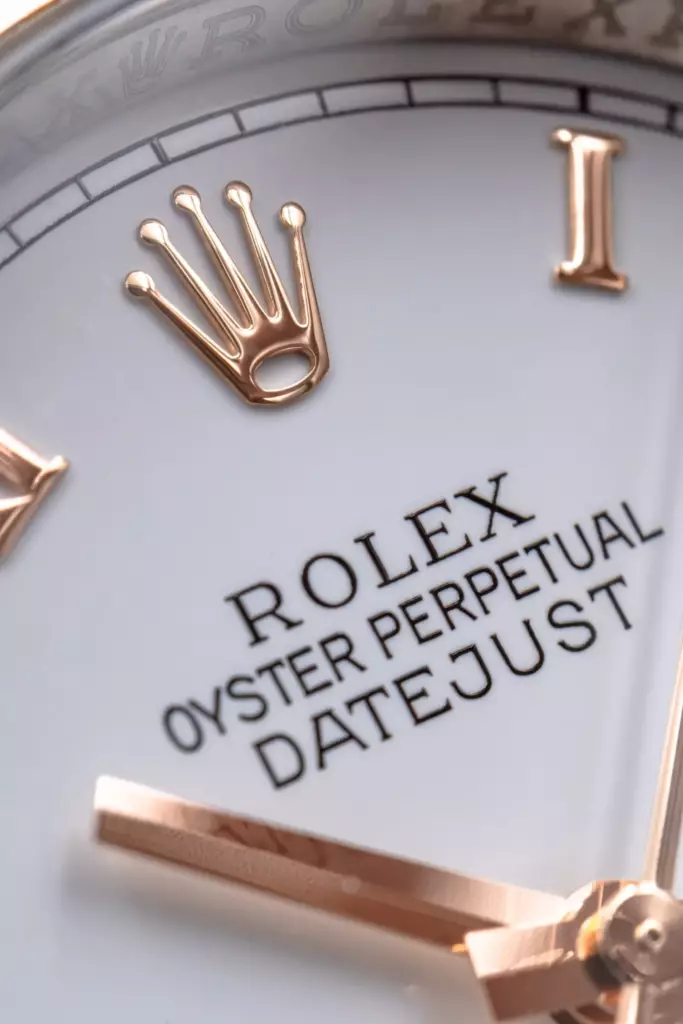 Macro du cadran d'une Rolex Datejust, couronne et index en or rose sur fond blanc laqué