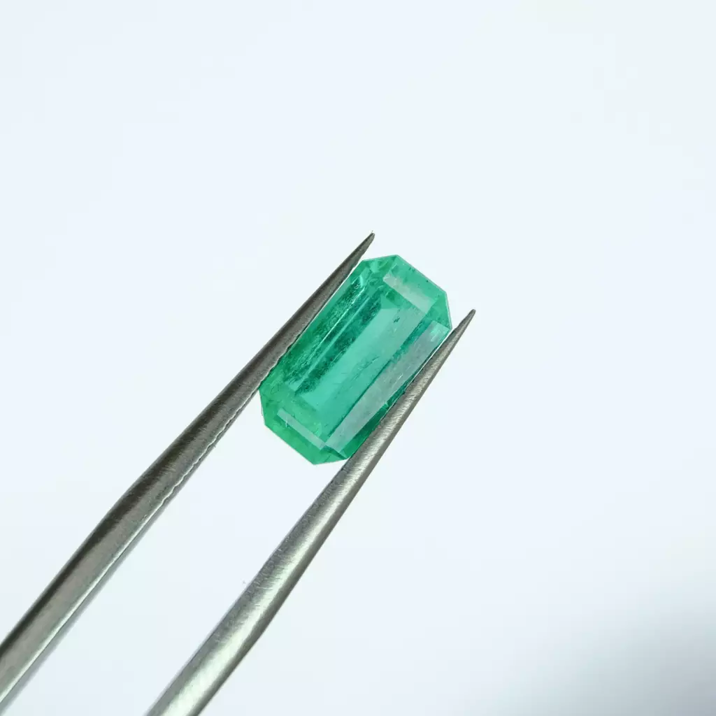 Émeraude rectangulaire vert d'eau tenue à la pince de gemmologue
