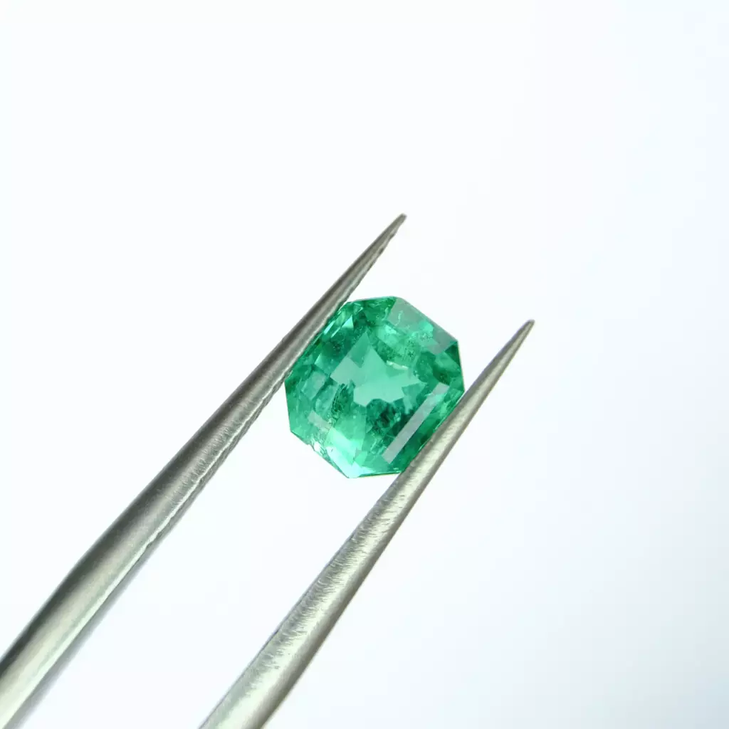 Émeraude taille carrée vert soutenu présentée à la pince de gemmologue