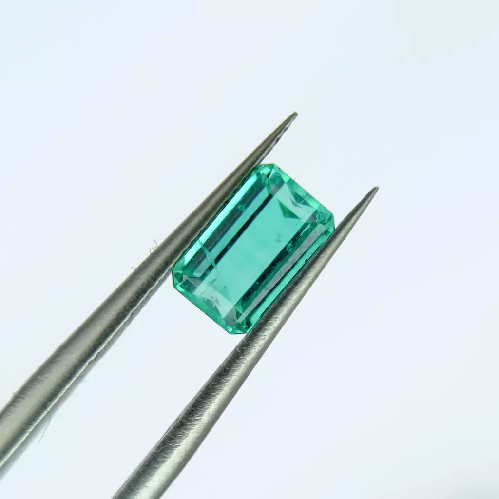 Émeraude taille émeraude tenue à la pince de gemmologue sur fond blanc